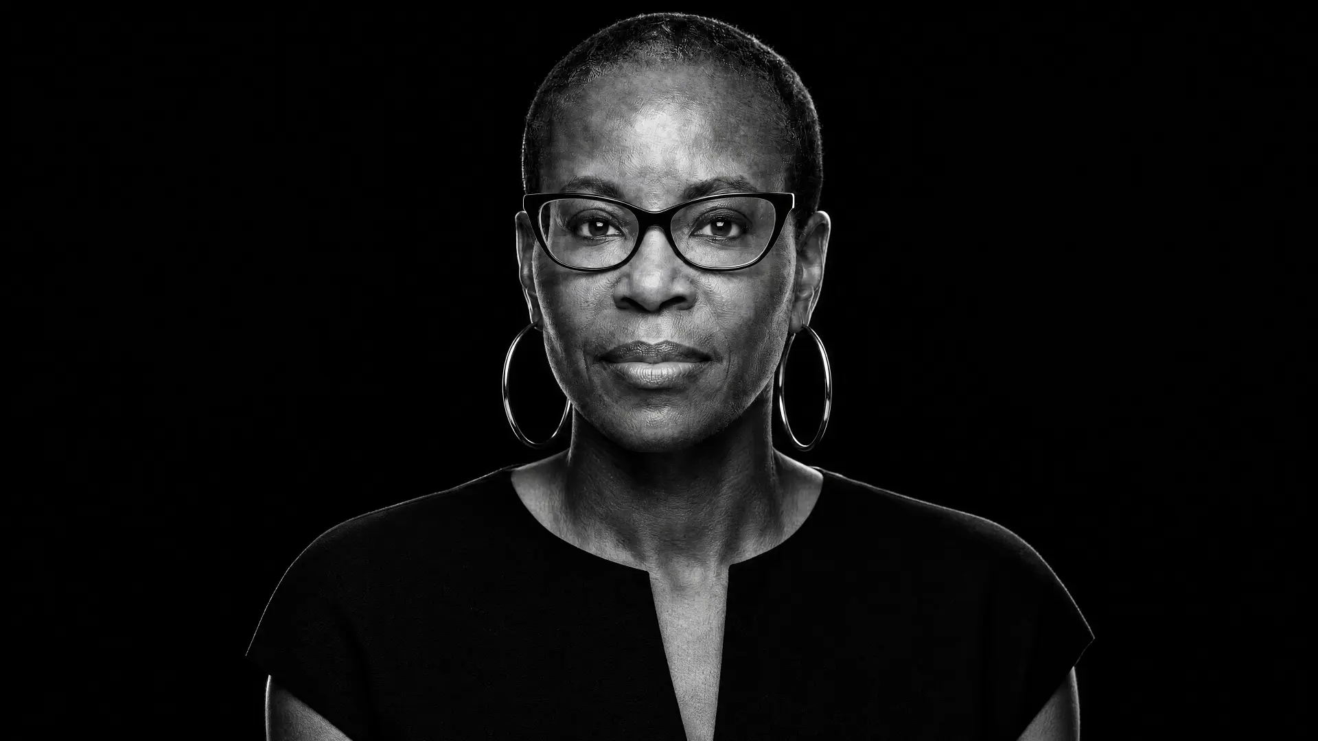 Nyia Harris portrait in black and white, wearing glasses and hoop earrings