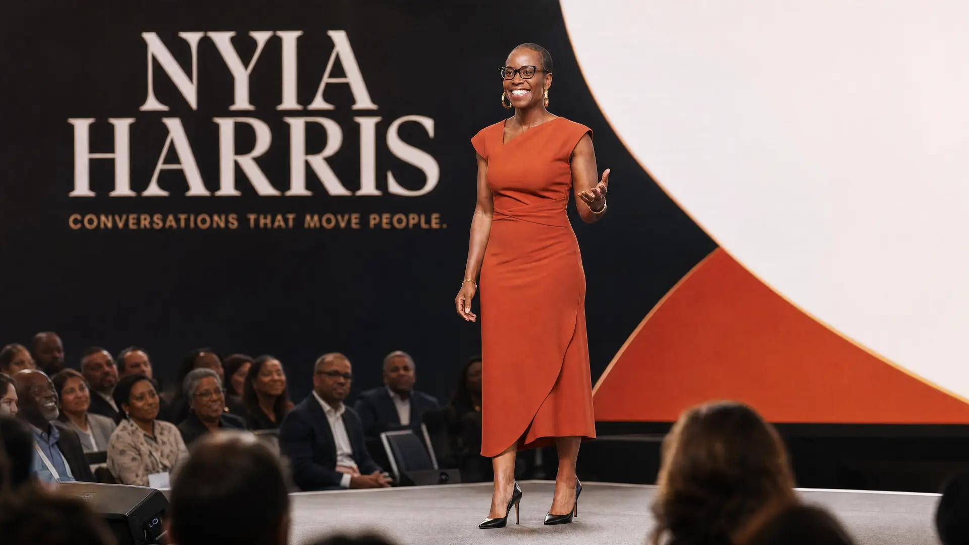 Nyia Harris on stage in a terracotta dress, speaking to an audience