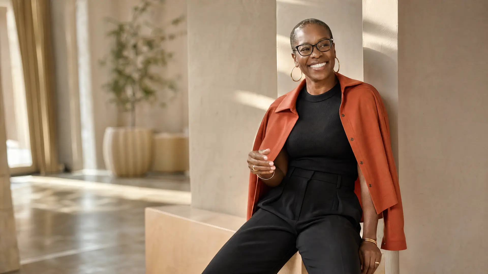Nyia Harris smiling in a warm modern corridor, wearing a terracotta jacket over black
